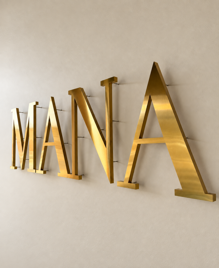 Gold MANA lettering mounted on a cream wall.