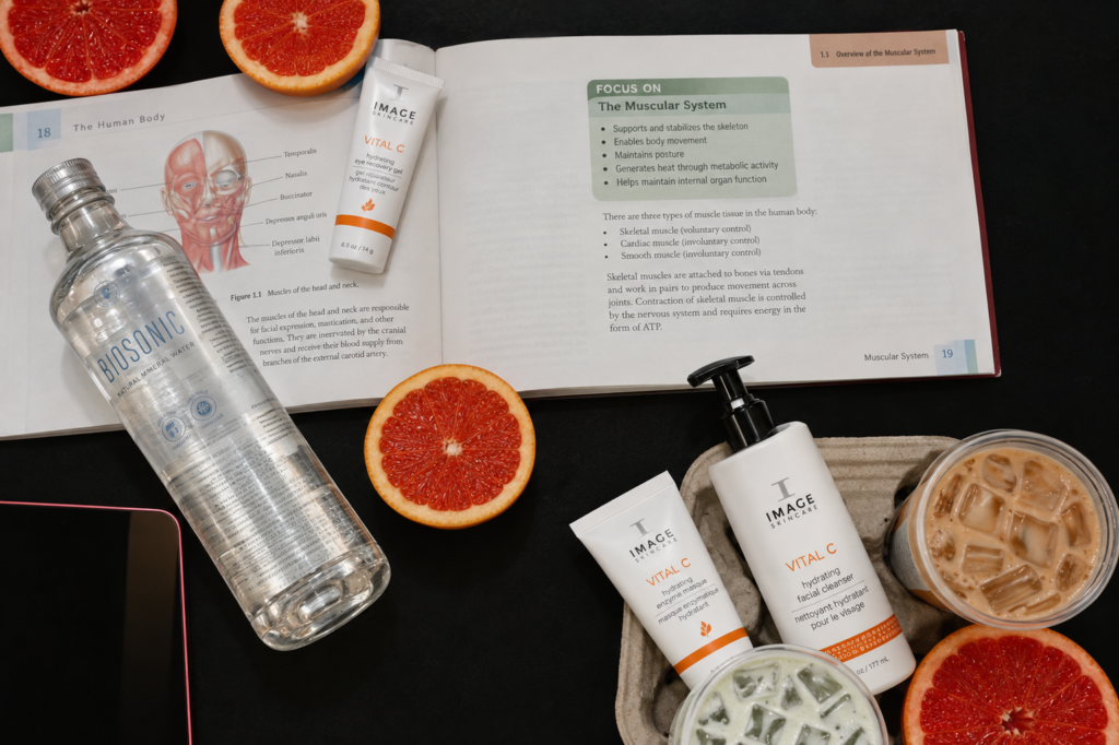 Open esthetics textbook showing facial muscles, surrounded by skincare products and grapefruit slices.